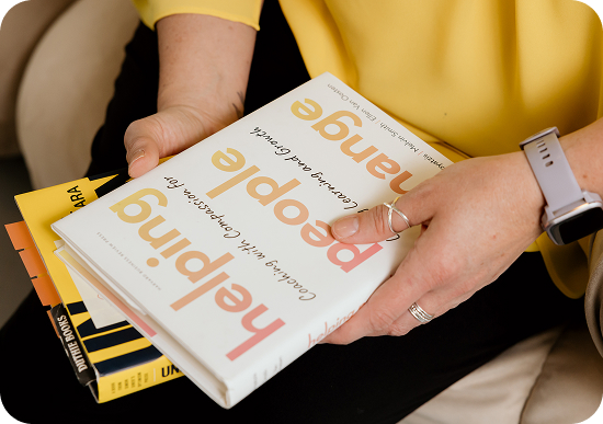 Hands holding hardcover books that appear to be for self help and professional development.